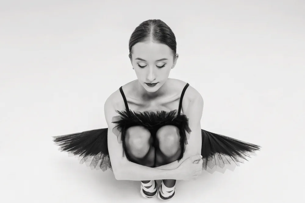 Alexandr: ein Porträt einer Ballerina in einem schwarzen Tutu,die hockt und ihre Knie umarmt