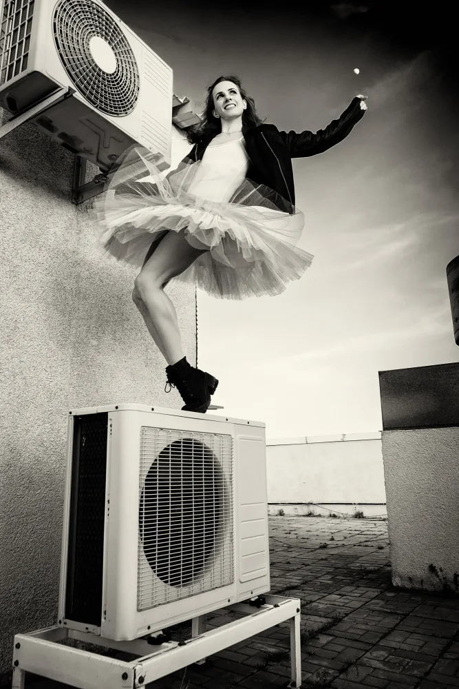 Alexandr: Eine Ballerina in Tutu,Jacke und Stiefeln klettert auf die Klimaanlage und posiert vor dem Himmel